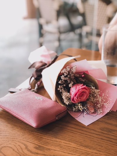粉红色的玫瑰花在棕色木桌上粉红色的马车皮夹旁
